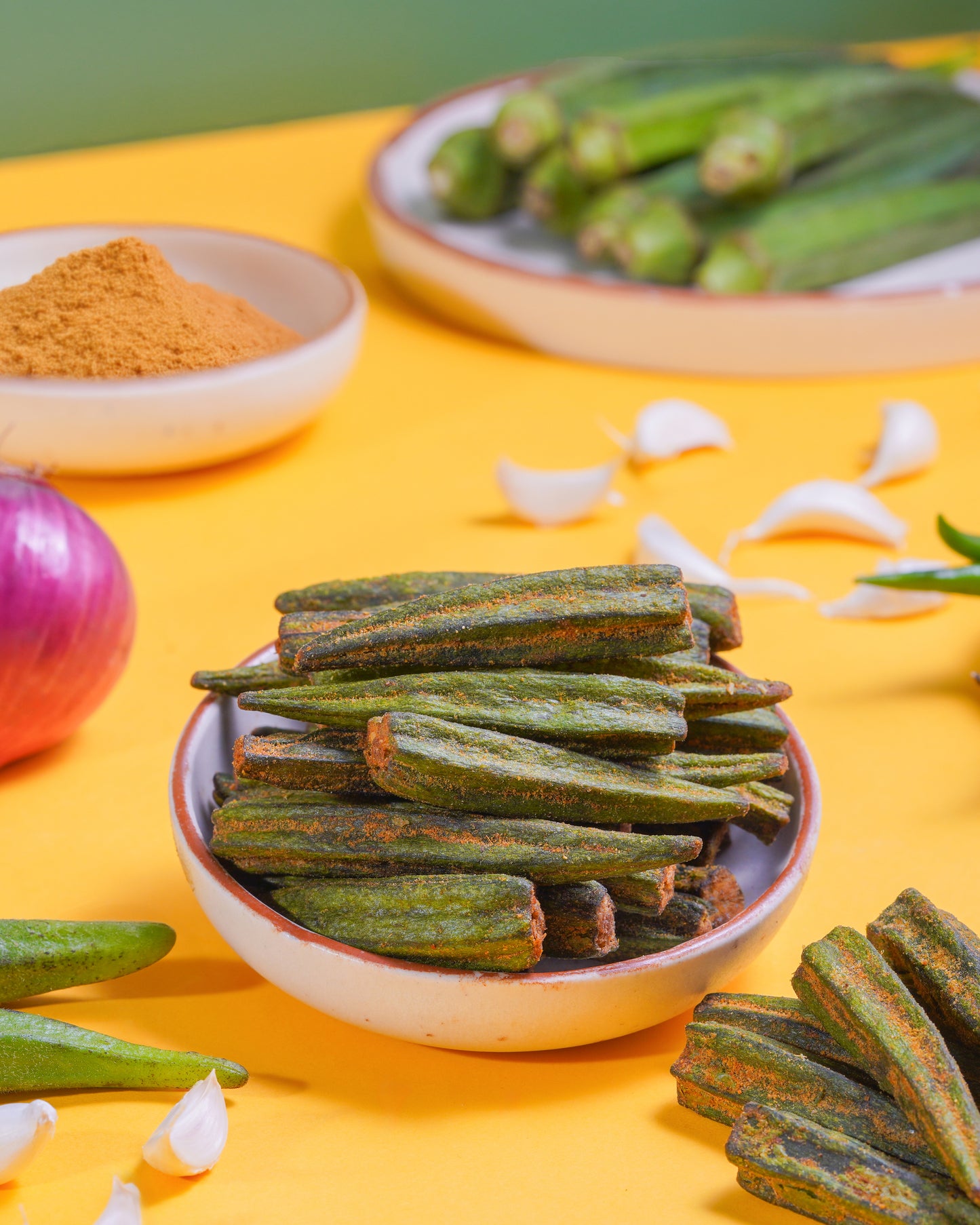 Bowl of okra with spices and ingredients on a yellow background