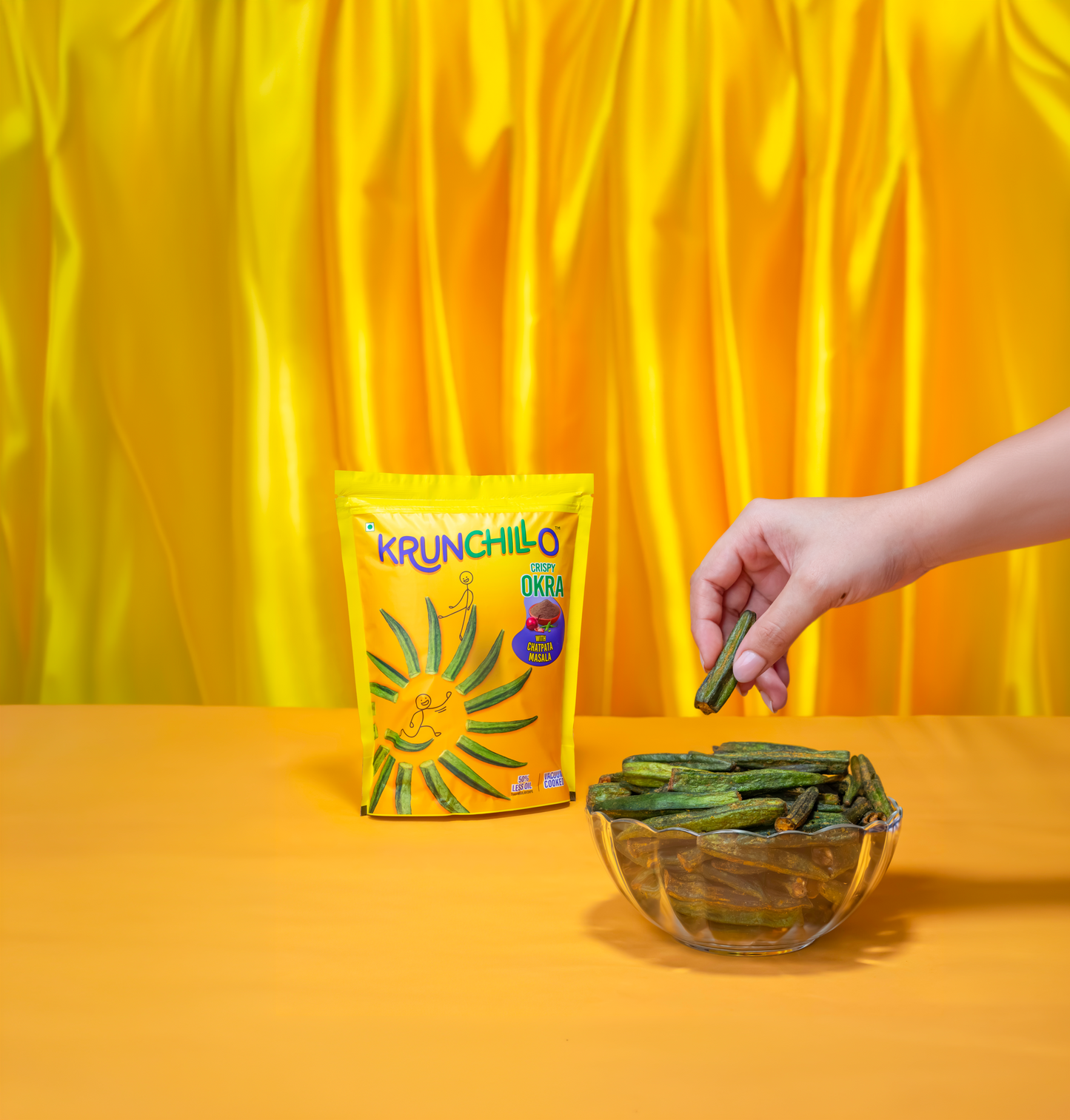 Hand picking green snacks from a bowl next to a Krunchilo bag against a yellow background